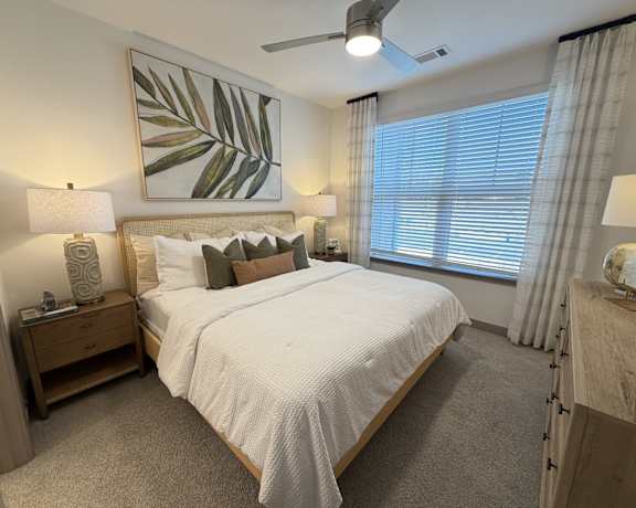 A bedroom with a large bed, a ceiling fan, and a painting on the wall.