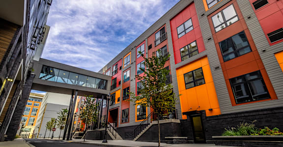 A modern building with orange and grey exterior and a tree in front at Center Square Lofts West, Allentown, PA