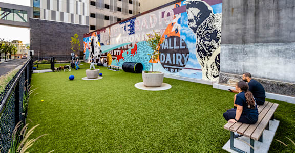 A man and woman sit on a bench in a grassy area with a mural on the wall at Center Square Lofts West, Allentown, PA