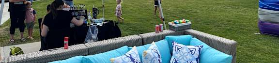 A blue canopy tent is set up in a grassy area with a couch and pillows underneath.