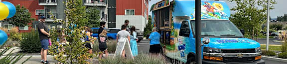 A blue ice cream truck is parked in front of a building with people standing around it.