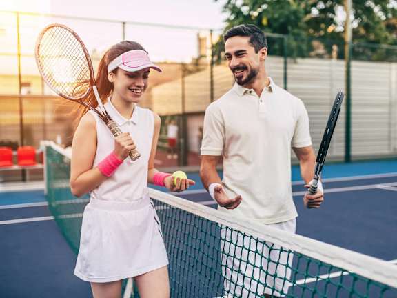 A man and a woman are standing on a tennis court, both holding tennis rackets and smiling at each other. at The Lex At Lowry, Denver, Colorado