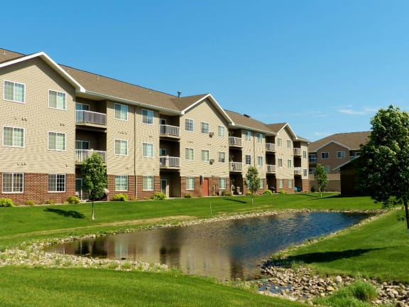an apartment building with a beautiful pond in front of it at Courtyard Apartments on Belsly, Moorhead, MN, 56560