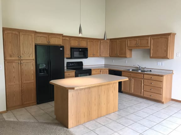 an empty kitchen with wooden cabinets and a black refrigerator