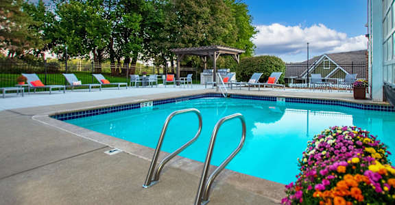 A pool with a diving board and chairs around it.