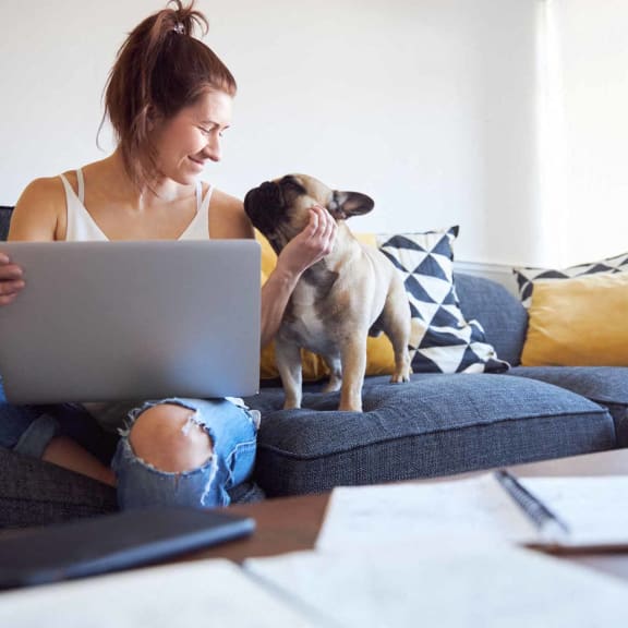 a woman sitting on a couch with a dog and a laptop