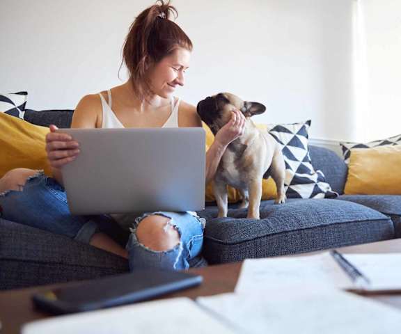 a woman sitting on a couch with a dog and a laptop