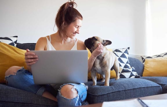 a woman sitting on a couch with a dog and a laptop