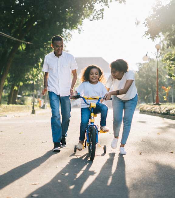 A family of three is walking together in a park with a child on a bicycle.