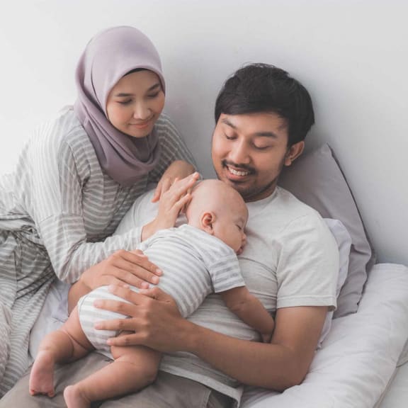 a man and woman sitting on a bed holding a baby