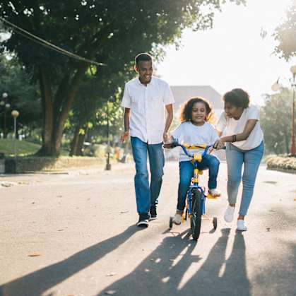 A family of three is walking together in a park with a child on a bicycle.