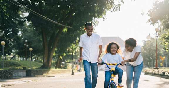 A family of three is walking together in a park with a child on a bicycle.