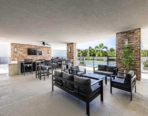 A modern outdoor patio with black furniture and a stone wall.