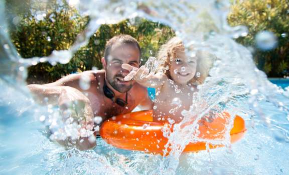 A man and a child are enjoying a splash in a pool.