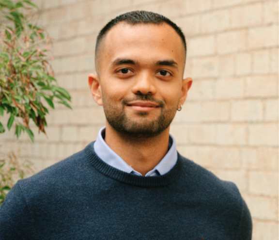 A man wearing a dark blue sweater with a small red logo on the left chest.