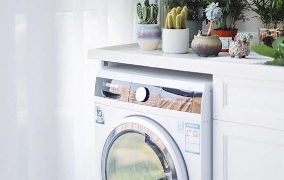 A white washing machine with a glass door is on a white cabinet.