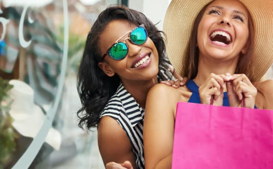 two women laughing while holding shopping bags