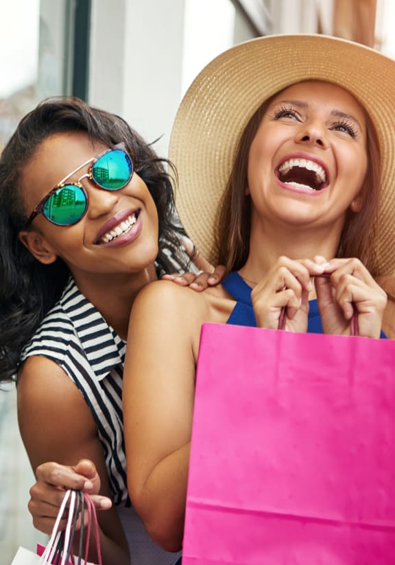 two women laughing while holding shopping bags