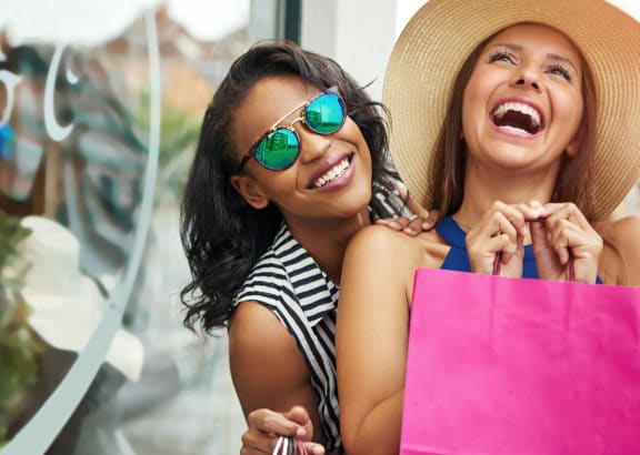 two women laughing while holding shopping bags