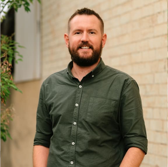 A man with a beard is smiling in front of a brick wall.