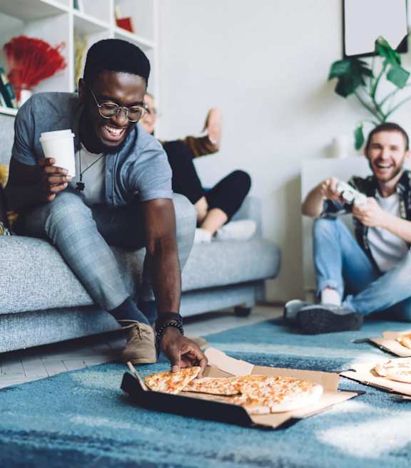 A man is sitting on the floor with a pizza box in front of him.
