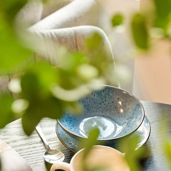 A cup of tea is on a saucer with a spoon on a wooden table.