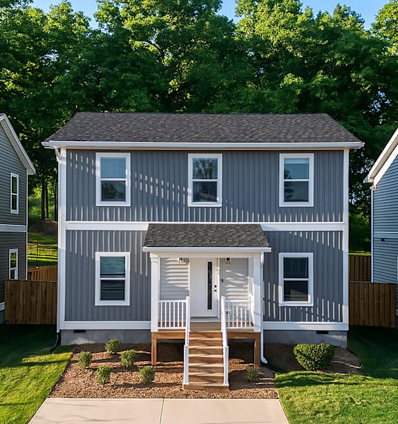 A modern two-story home with a green exterior, white trim, a covered front porch, and a neatly landscaped yard in a suburban neighborhood.