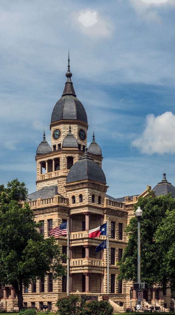 a large building with a clock tower and trees in front of it  at Alta Denton Station, Denton, Texas