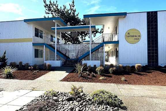 A white building with a blue roof and a sign that says "Tamarack 702" is shown.