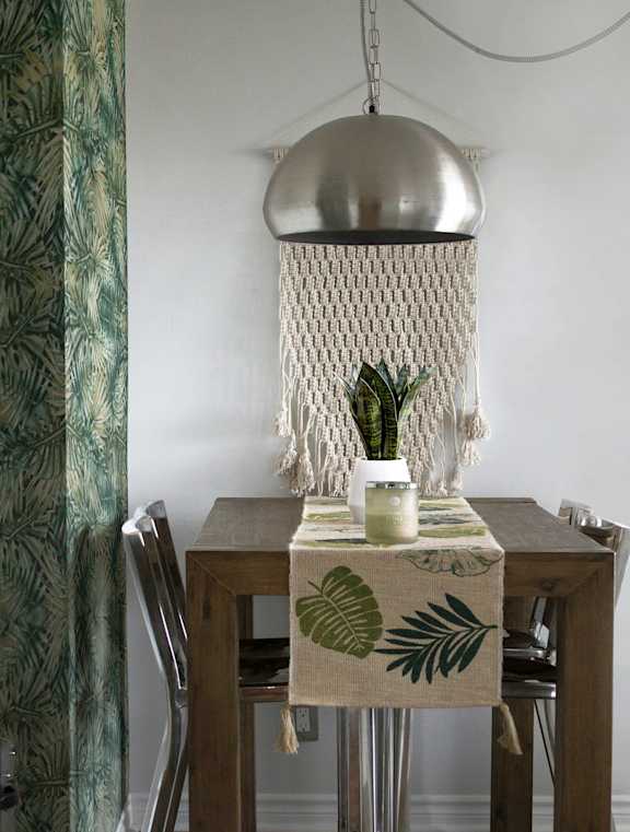 A dining table with a leaf patterned cloth and a plant on it.