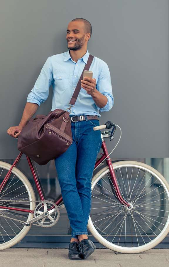 Man Smiling and Holding Phone while Standing Next to Bike
