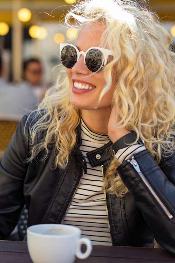 Woman Smiling while Sitting Outside and Wearing Sunglasses and Black Jacket