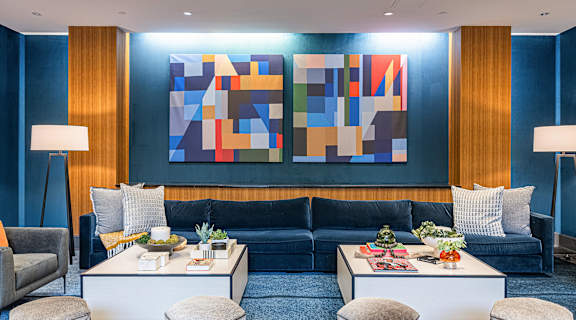 a living room with blue walls and furniture and a colorful wall art
