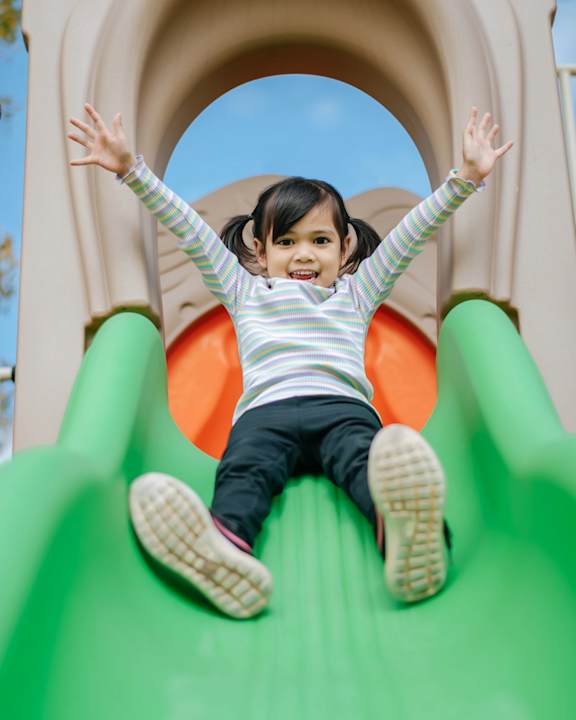 A little girl is sliding down a green slide.