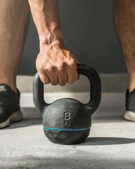 A person's hand is holding a black kettlebell with the number 8 on it.