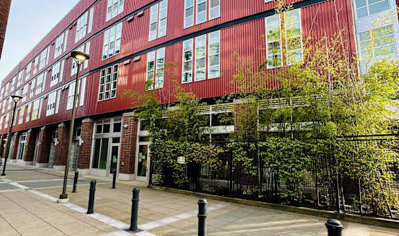 A red building with a black fence and trees in front.