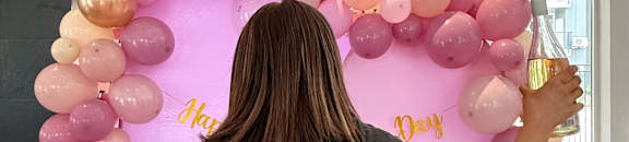 A woman in a black t-shirt with the text "32 Below" is standing in front of a balloon arch.