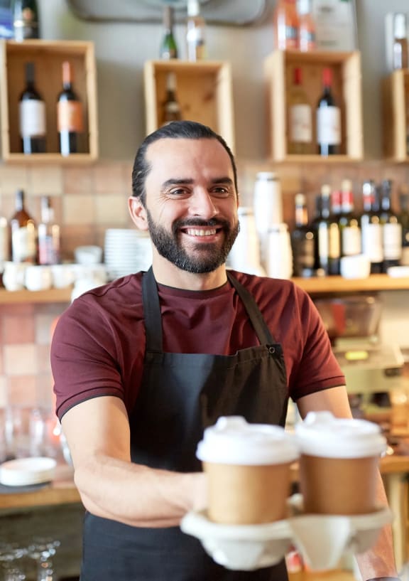 a man in an apron holding a stack of coffee cups