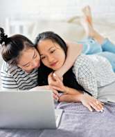Two women are lying on a bed with a laptop.