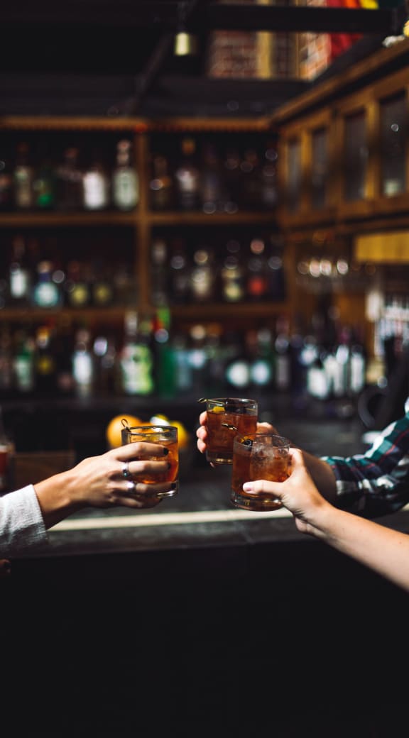 two people holding up glasses of whiskey at a bar