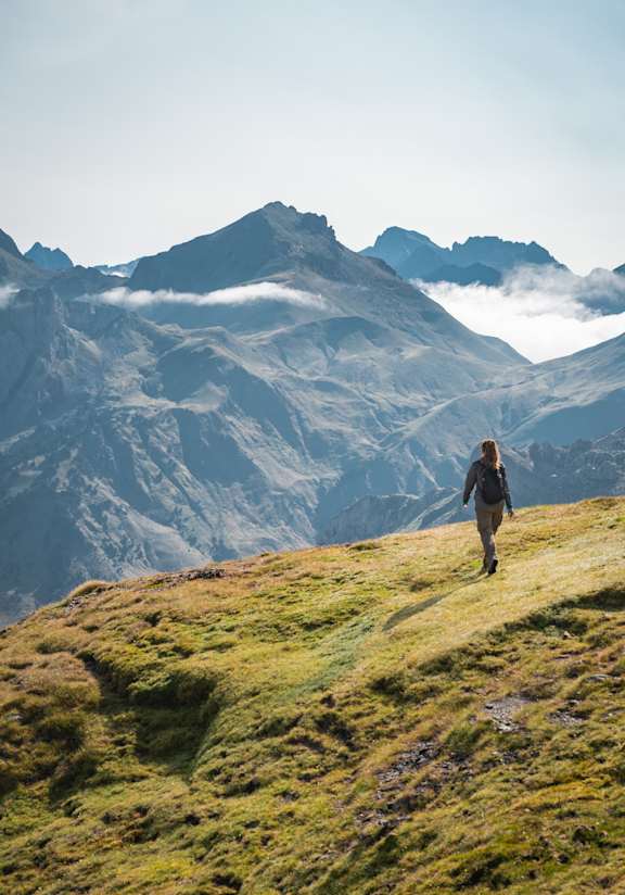 Woman Hiking on Grassy Hill with Mountains in the Background
