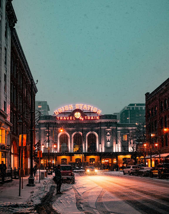 A snowy street with a brightly lit Travelers Theatre marquee.