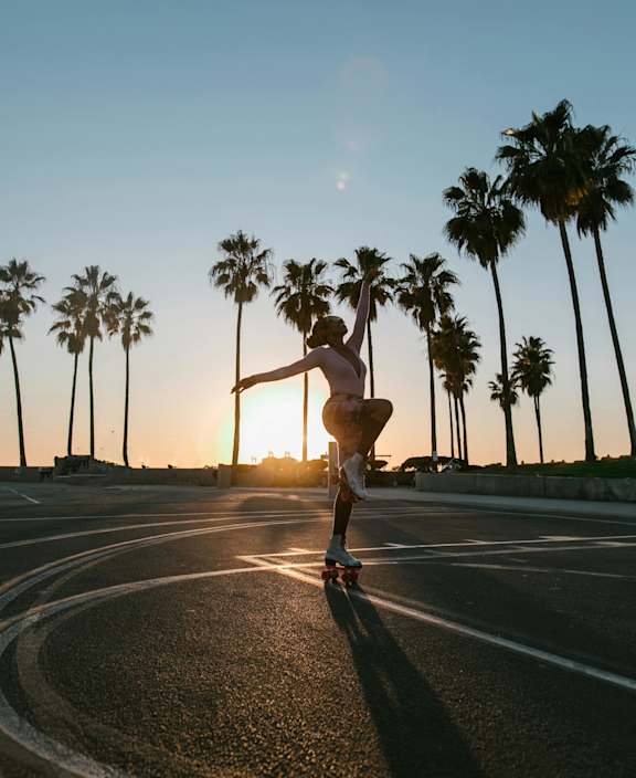 A person is skateboarding on a road with palm trees and a bird flying in the sky.