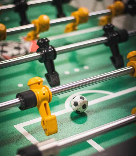 A foosball table with a soccer ball on the green playing surface.