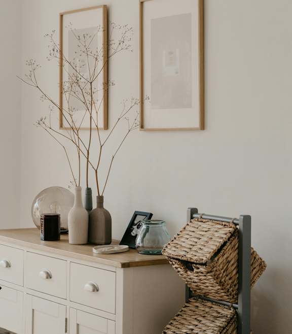 A white dresser with a wicker basket on top and two framed pictures on the wall.