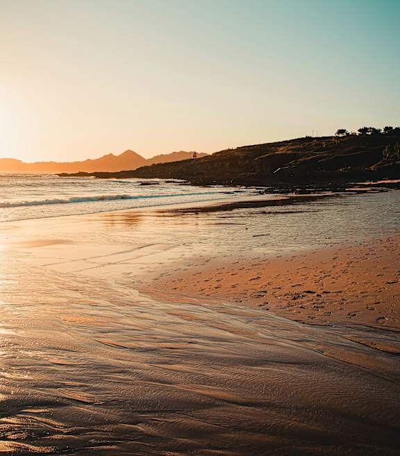 A person is walking on the beach with a surfboard.