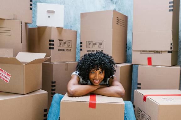 A person is sitting on a cardboard box surrounded by other boxes.