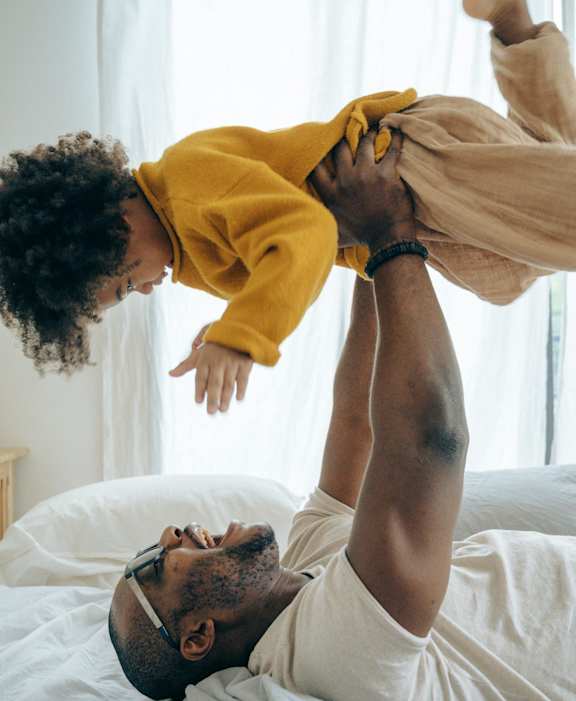 A man lifts a child in the air while lying on a bed.