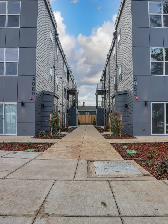a pathway between two apartment buildings with a cloudy sky in the background