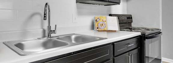A kitchen with a stainless steel sink and black cabinets at 46Eleven Apartments, Dallas, TX, 75228